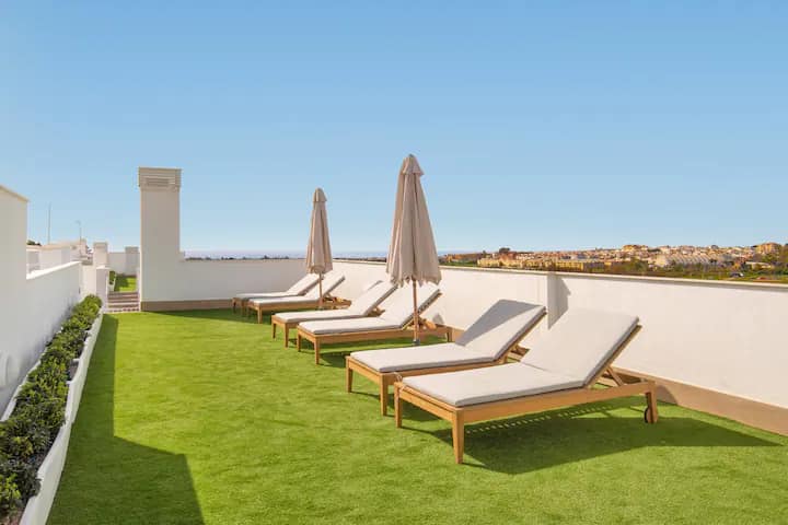 Daktuin van Residencia Jardin del Rio met ligstoelen en zeezicht, Nueva Andalucía